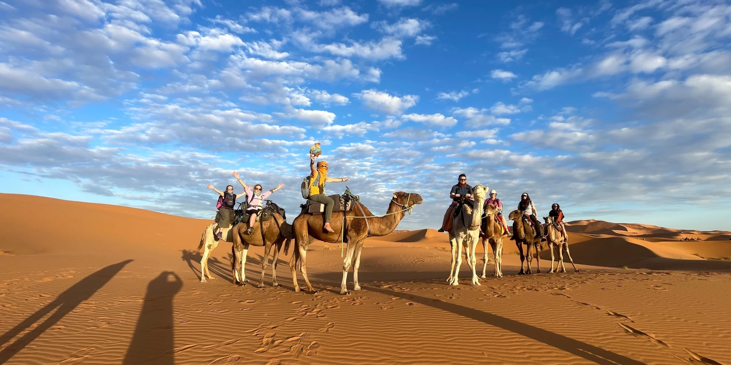 A group of adventurers riding camels in the Sahara Desert on the Morocco Adventure Tour